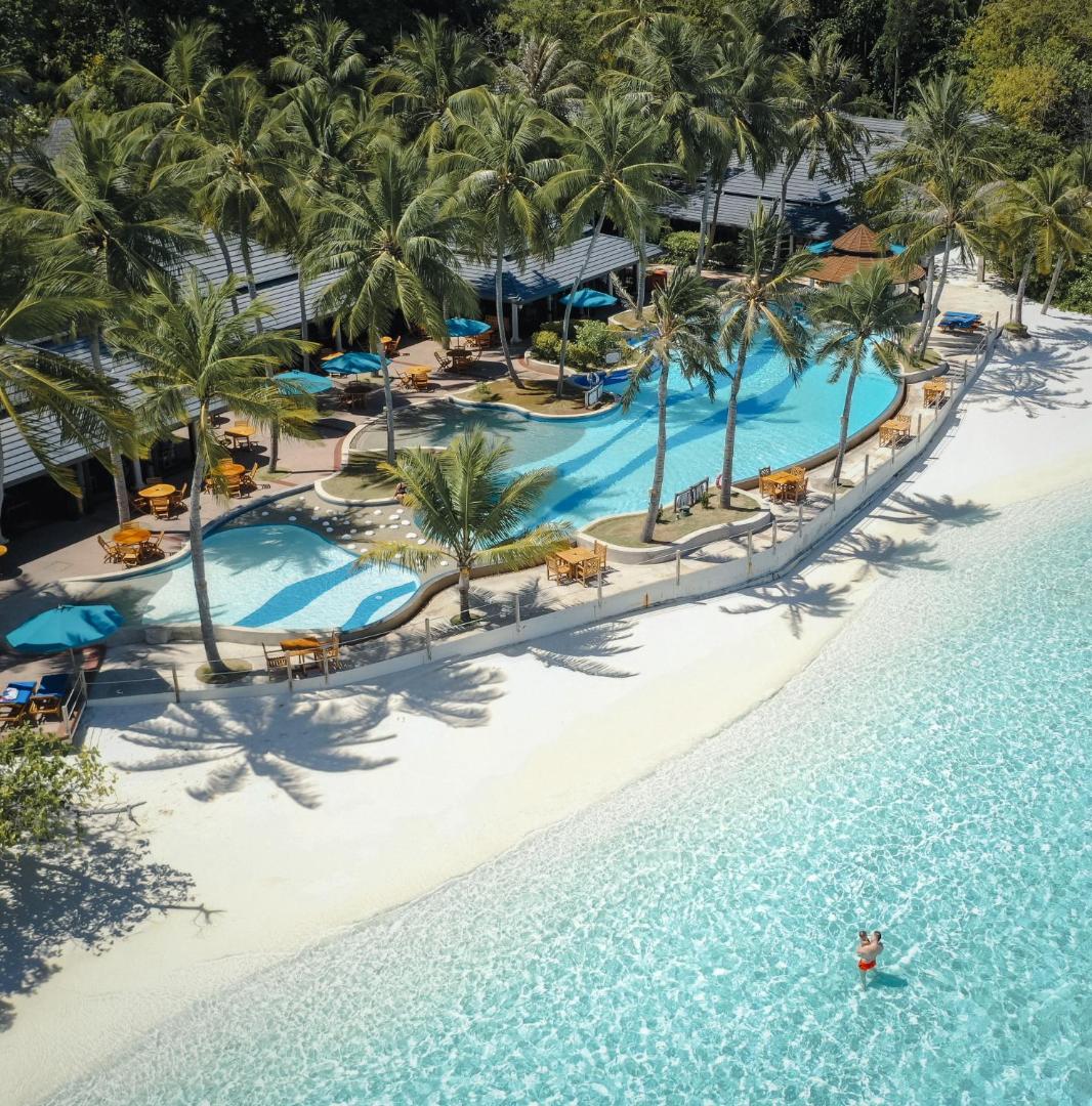 Royal Island Resort & Spa pludmales zona ar baseinu, restorāna galdiņiem zem palmām un dzidru okeāna ūdeni Maldivu salās