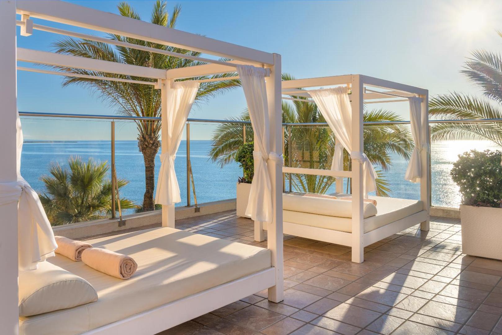 Grezni balti atpūtas guļamkrēsli uz Elba Estepona Gran Hotel terases ar skatu uz Vidusjūru un palmām