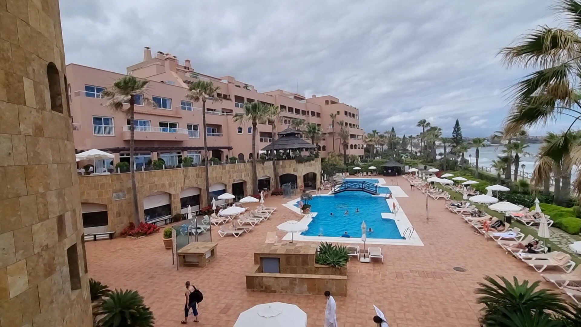 Elba Estepona Gran Hotel And Thalasso Spa centrālais baseins ar tiltiņu, sauļošanās zonu un viesnīcas fasādi mākoņainā dienā