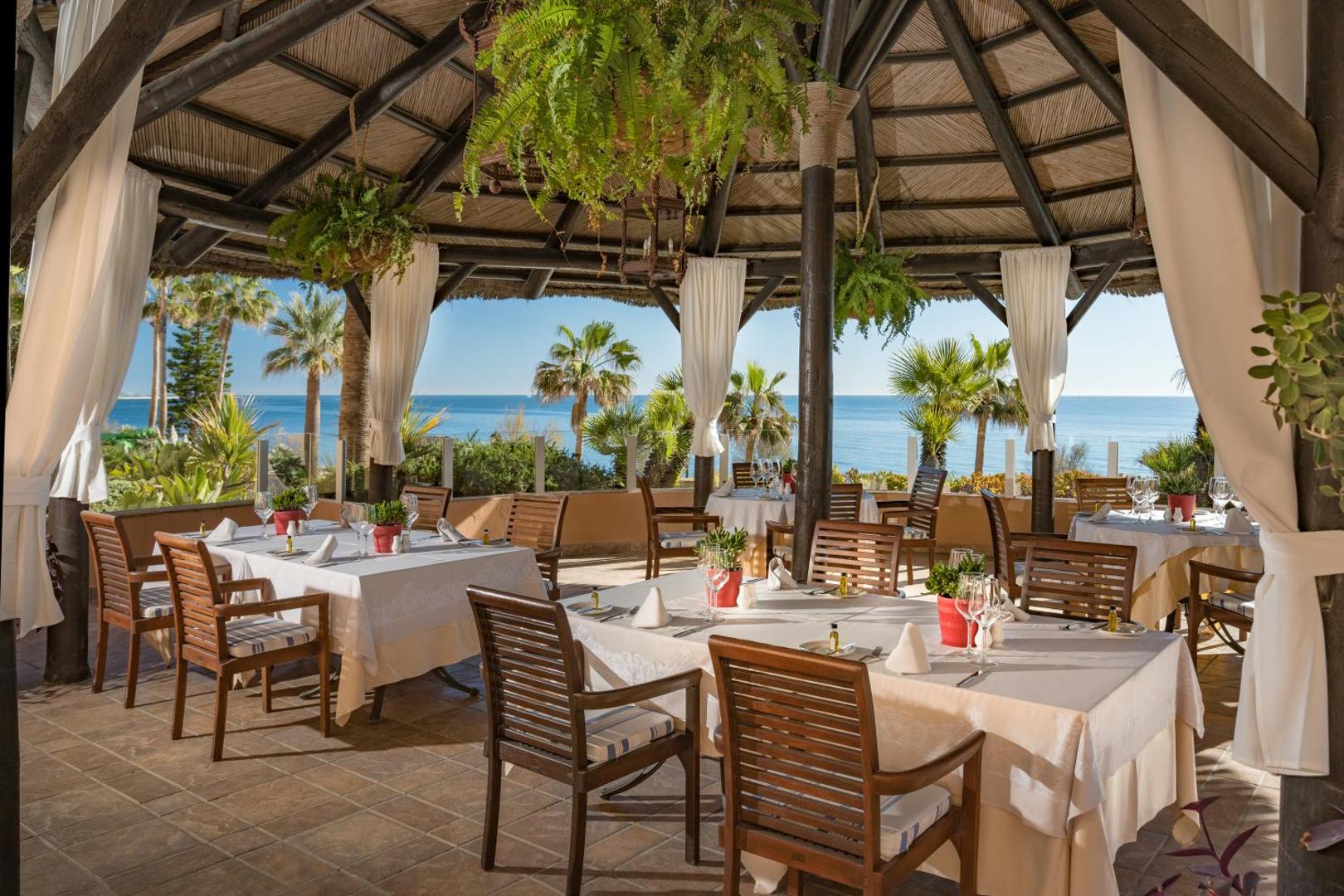 Elba Estepona Gran Hotel restorāna āra terase ar skatu uz Vidusjūru Esteponā — eleganti klāti galdi zem koka nojumes ar palmām