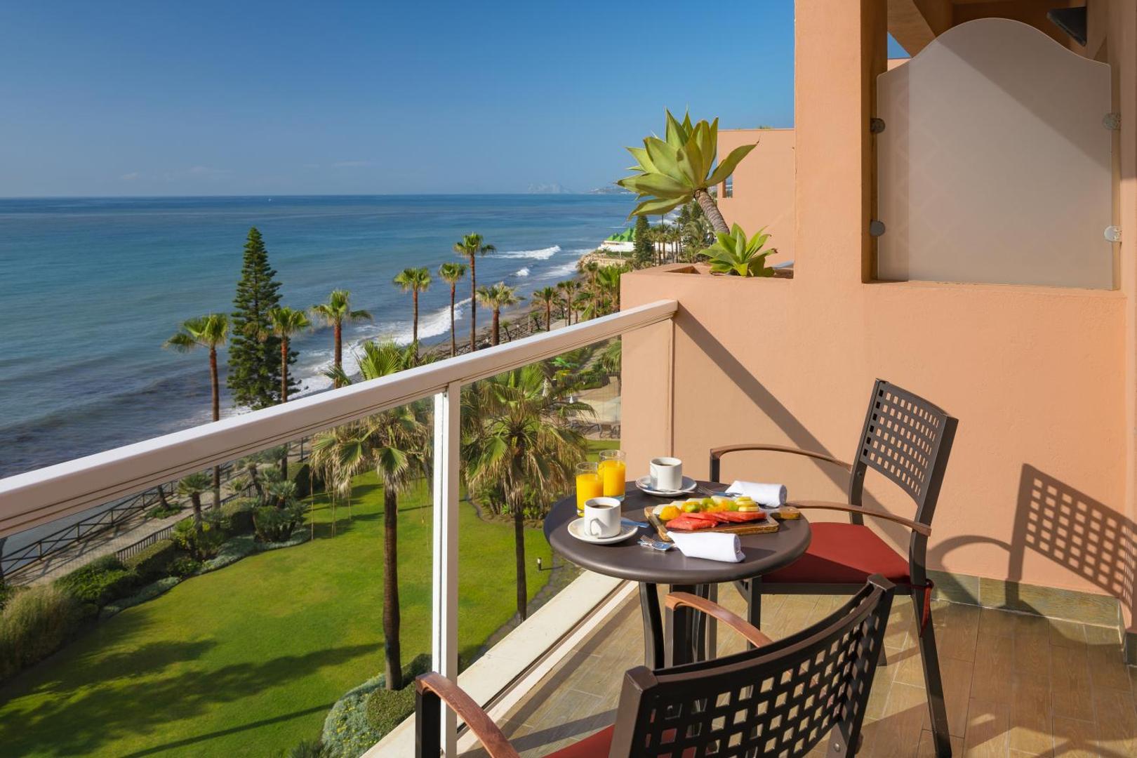 Skats no Elba Estepona Gran Hotel numura balkona uz jūru un dārzu, uz galda servētas brokastis un augļi