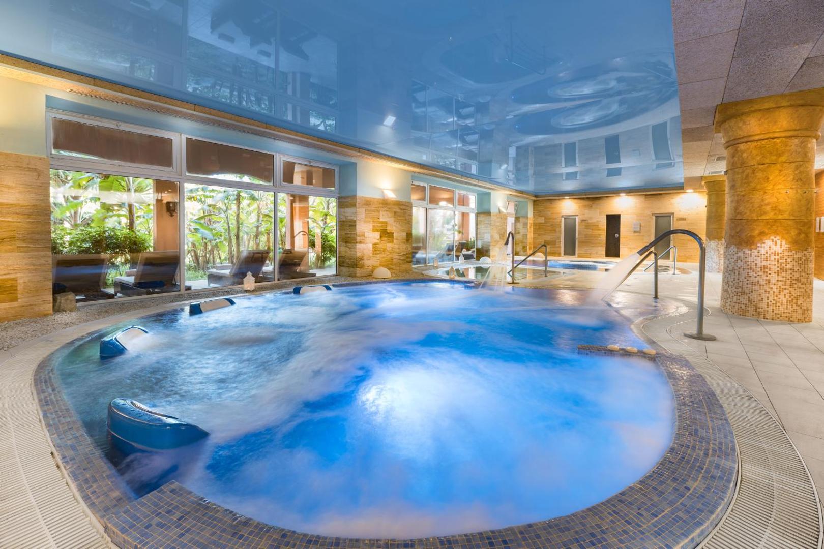 Elba Estepona Gran Hotel Thalasso Spa modernais hidromasāžas baseins ar zilu apgaismojumu un skatu uz dārzu caur lieliem logiem
