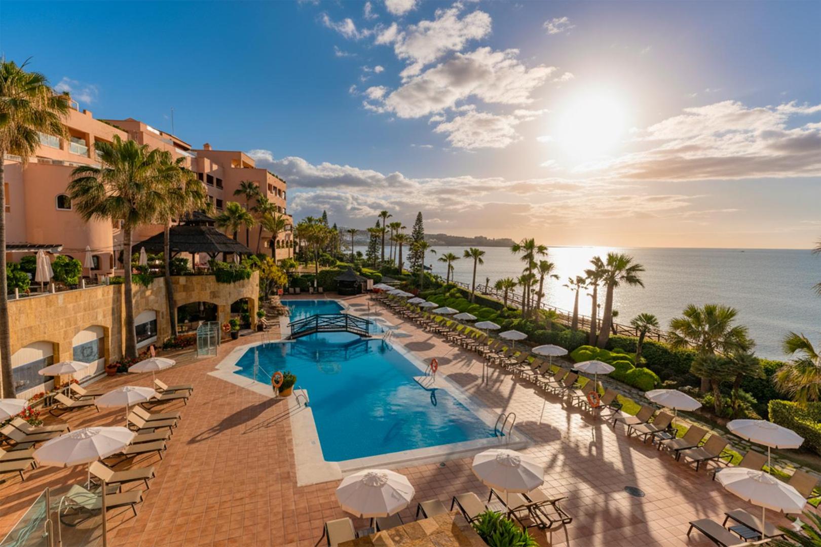 Elba Estepona Gran Hotel And Thalasso Spa āra baseina zona saulrietā ar palmām, sauļošanās krēsliem un skatu uz jūru