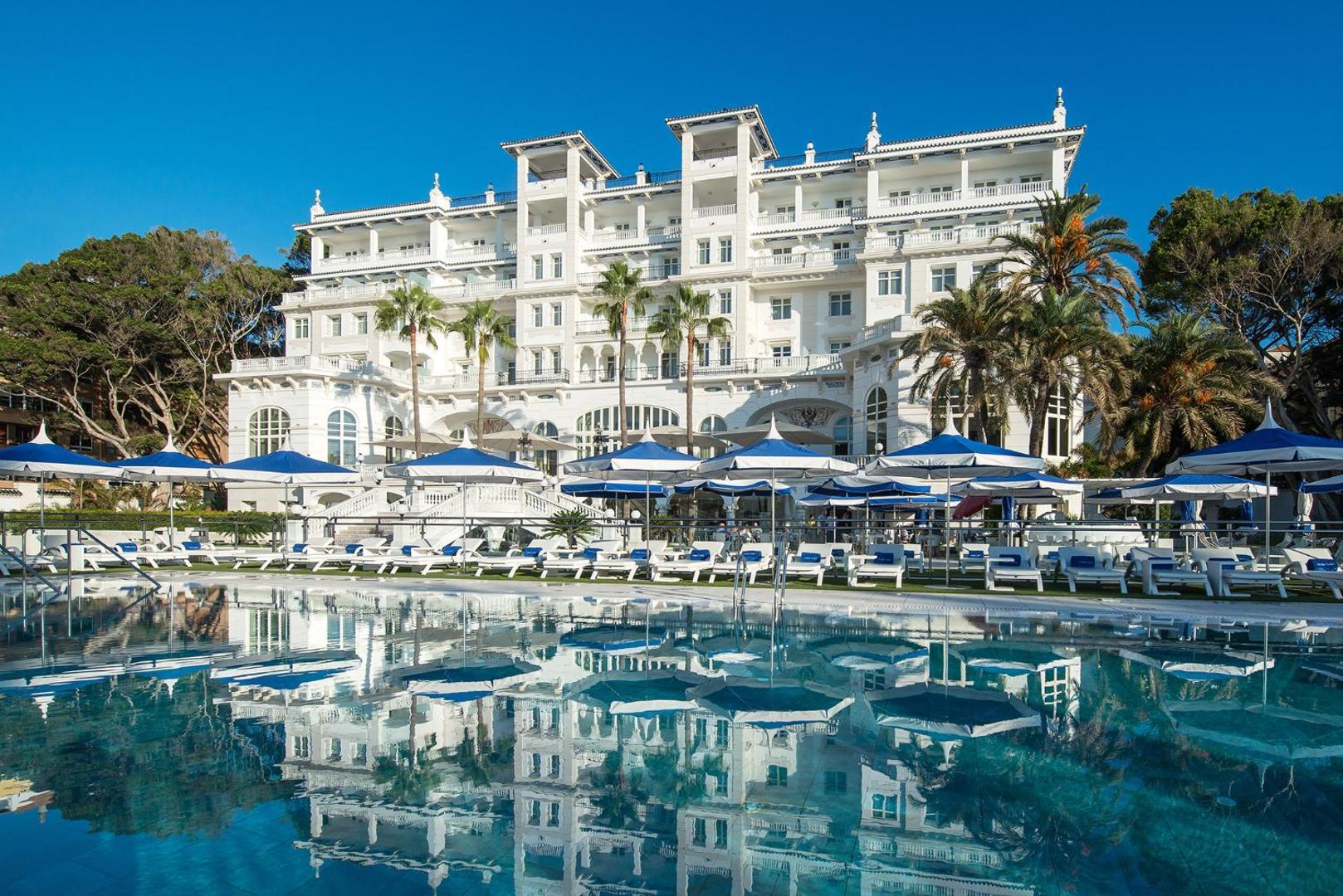 Gran Hotel Miramar fasāde Malagā ar lielu āra baseinu, ziliem saulessargiem un vēsturisku arhitektūru saulainā dienā Spānijā
