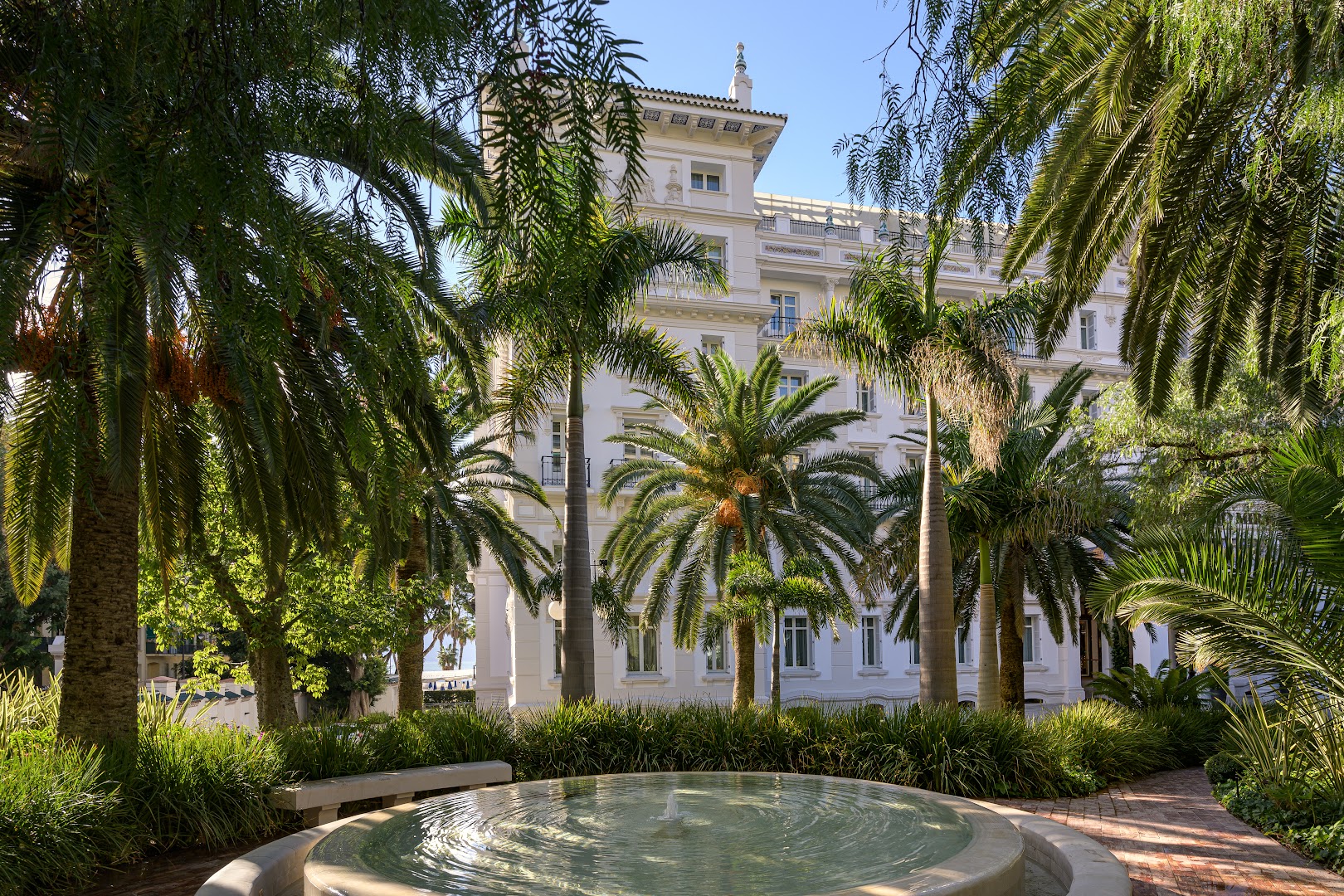 Gran Hotel Miramar dārza strūklaka palmu un zaļumu ielenkumā Malagā — mierpilna atpūtas zona pie vēsturiskās viesnīcas ēkas
