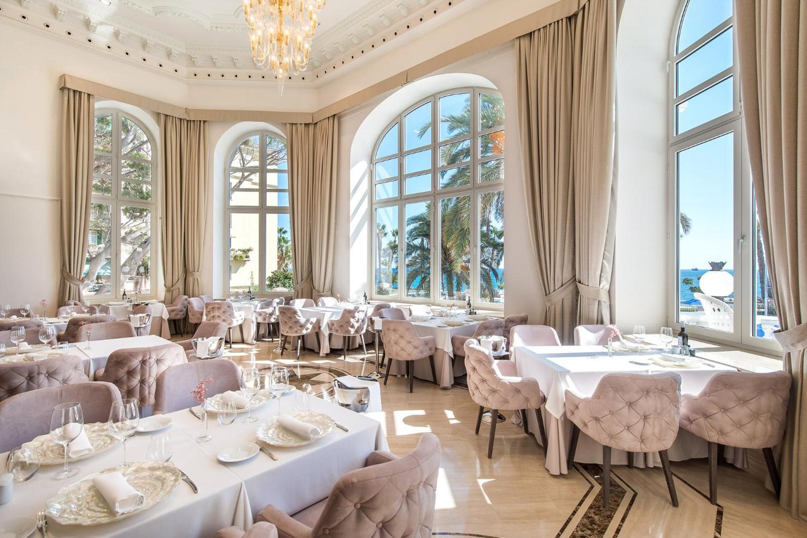 Gran Hotel Miramar restorāna zāle ar augstiem griestiem, lieliem logiem un skatu uz palmām Malagā, Spānijā