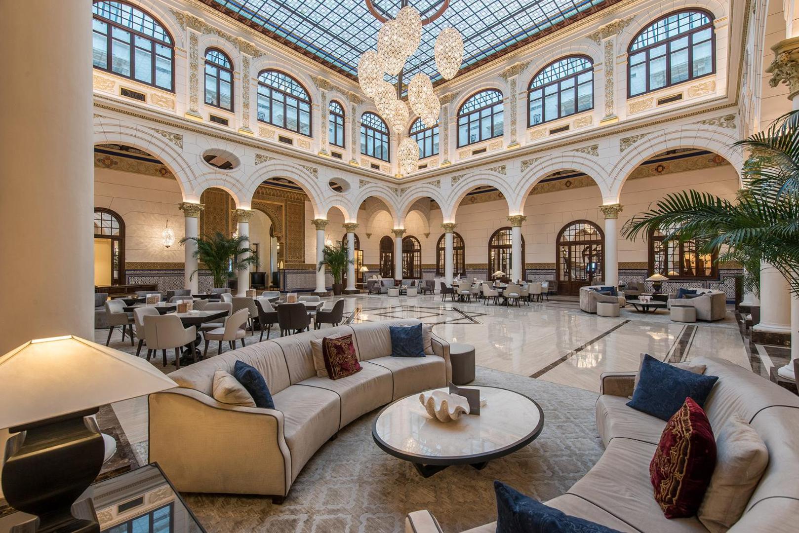 Gran Hotel Miramar iespaidīgais vestibils ar stikla griestiem, arkām, palmām un greznām lustrām Malagā