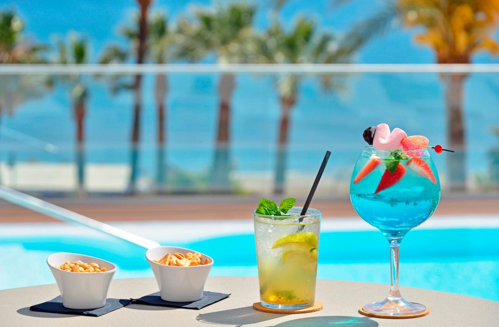 Eksotiski kokteiļi un uzkodas pie Sol House Costa Del Sol baseina ar skatu uz palmām un Vidusjūras piekrasti