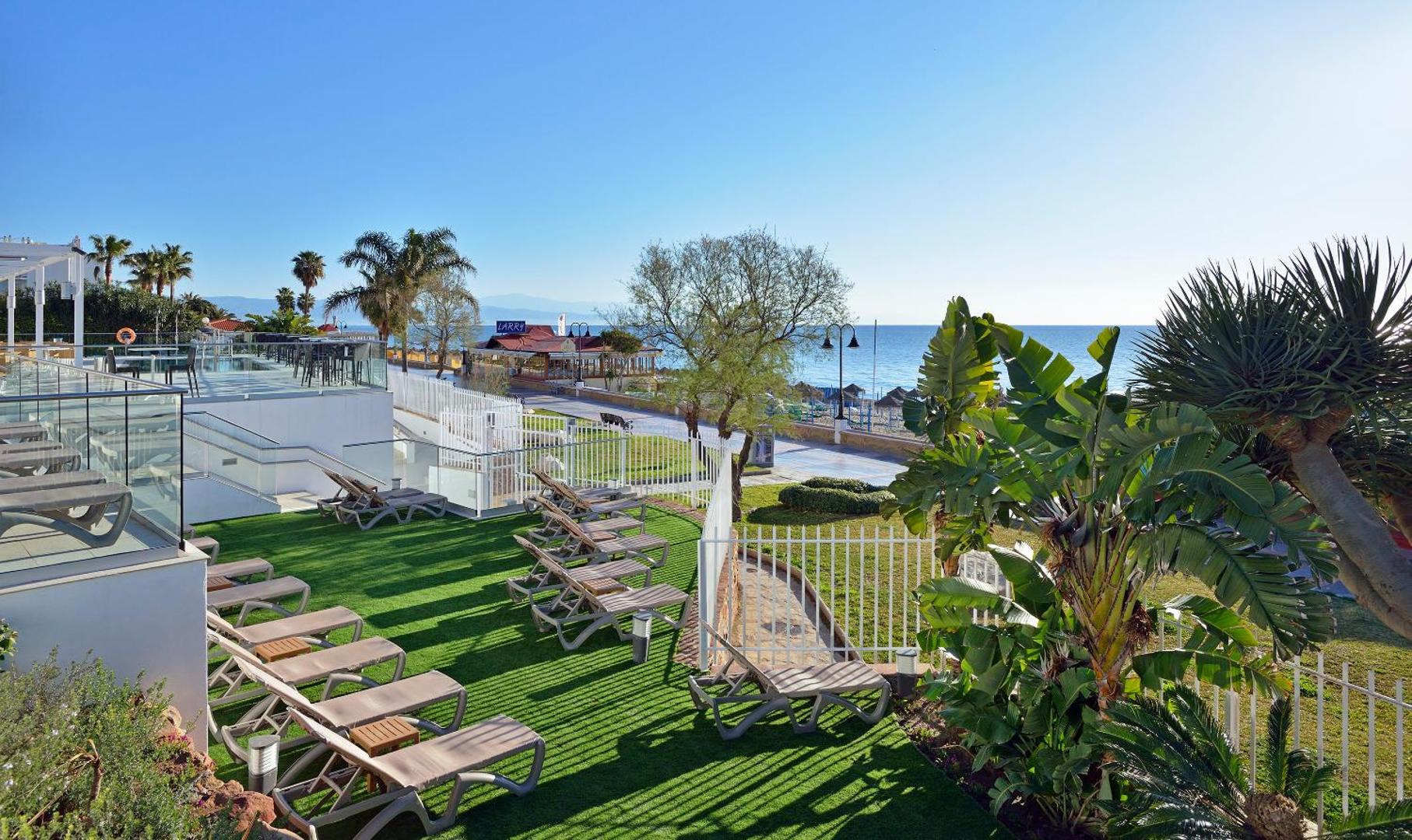 Sol House Costa del Sol āra terase ar sauļošanās krēsliem uz mākslīgā zālāja, skats uz jūru un palmām Torremolinosā, Spānijā