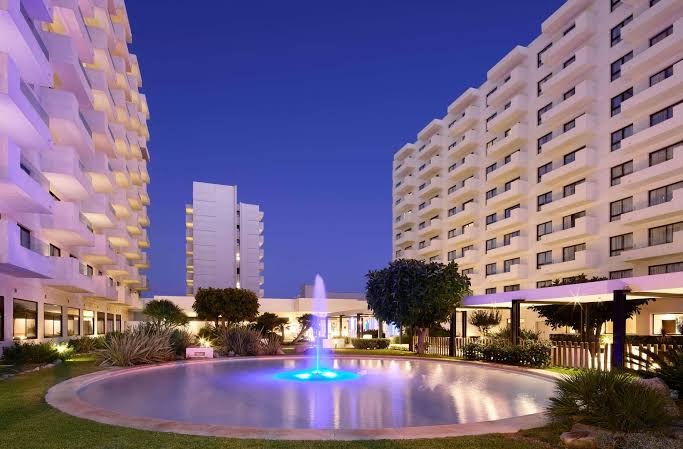 Sol House Costa del Sol centrālā strūklaka ar zilu apgaismojumu nakts laikā, fonā viesnīcas korpusi ar balkoniem