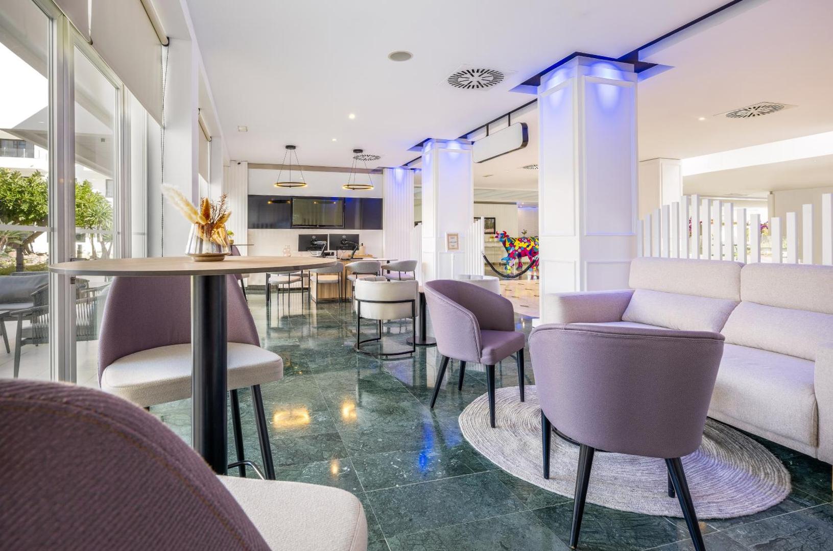 Sol House Costa Del Sol gaišā lobby zona ar violetiem atpūtas krēsliem, lieliem logiem un modernu interjeru Spānijas piekrastē
