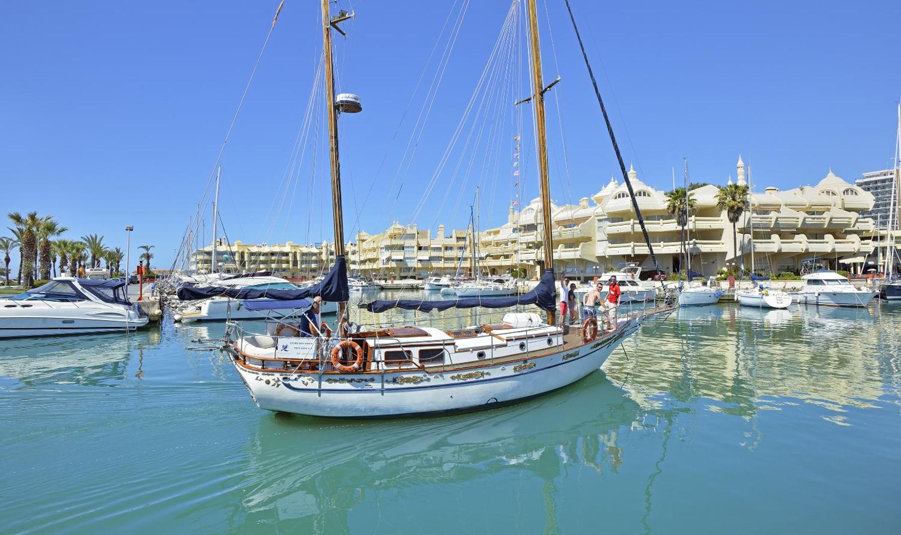 Skats uz Sol House Costa Del Sol viesnīcas ēku no jahtu piestātnes ar baltu buru kuģi priekšplānā