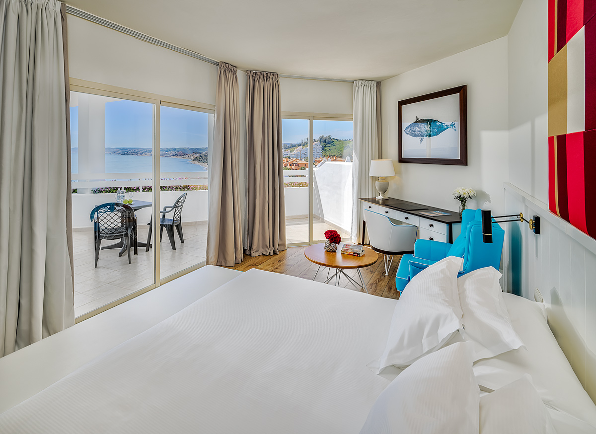 H10 Estepona Palace gaišs numurs ar lielu gultu, atpūtas zonu un plašu terasi, no kuras paveras skats uz Vidusjūru.