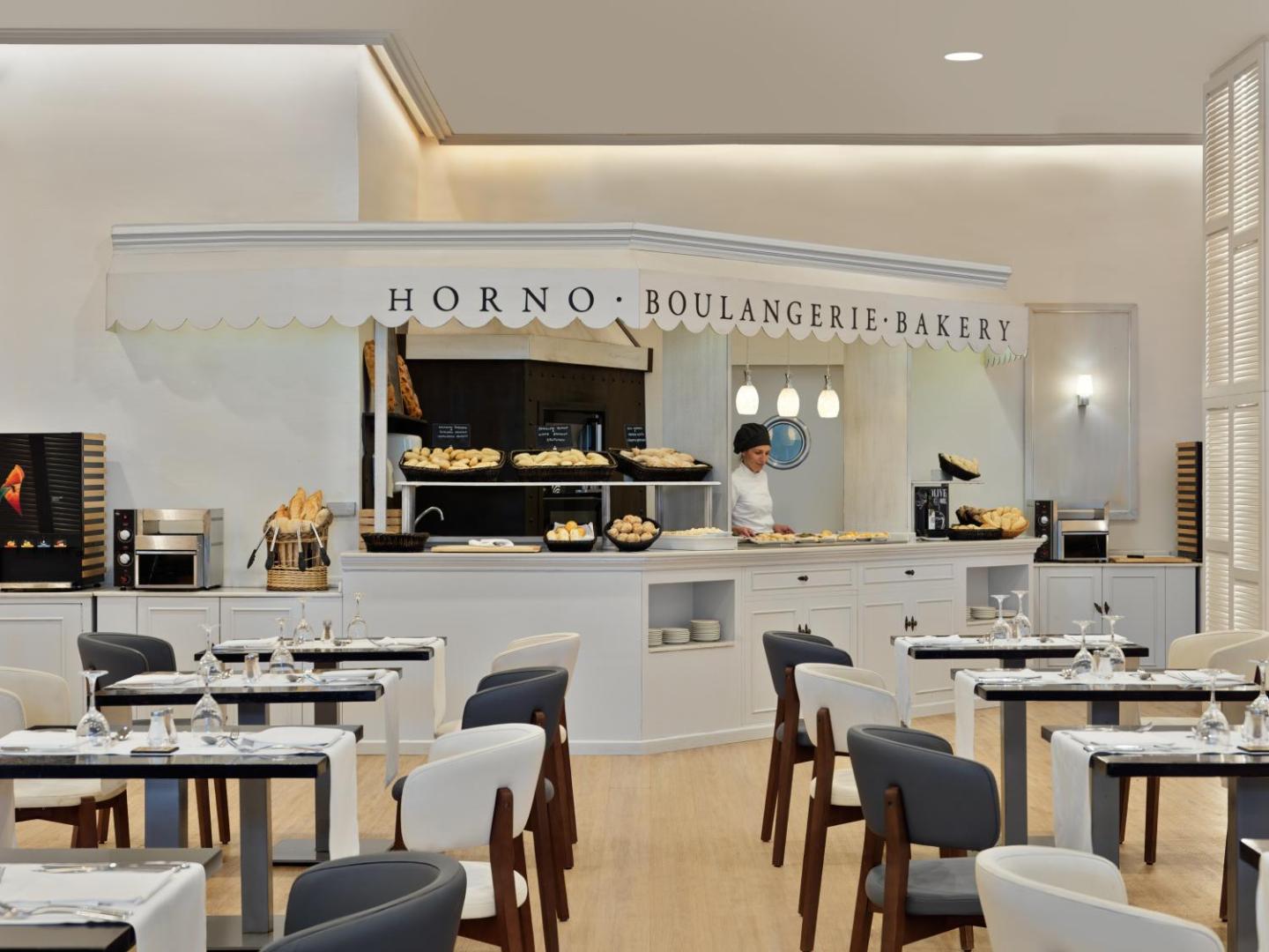 H10 Estepona Palace restorāna maizes stūrītis Horno Boulangerie Bakery ar svaigiem konditorejas izstrādājumiem un galdiņiem priekšplānā.