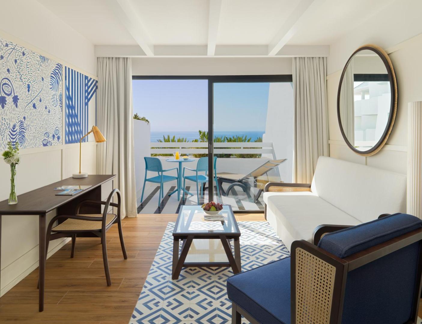 H10 Estepona Palace viesistabas zona ar modernu dīvānu, darba galdu un skatu uz Vidusjūru caur stikla durvīm