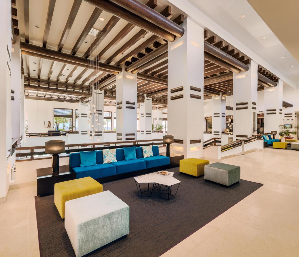 H10 Estepona Palace viesnīcas vestibils ar augstiem griestiem, koka sijām, modernām mēbelēm un zilām sofām atpūtas zonā