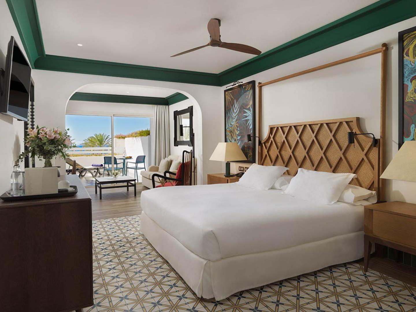 H10 Estepona Palace viesnīcas numurs ar lielu gultu, pītu galvgali un izeju uz saulainu terasi ar skatu uz jūru