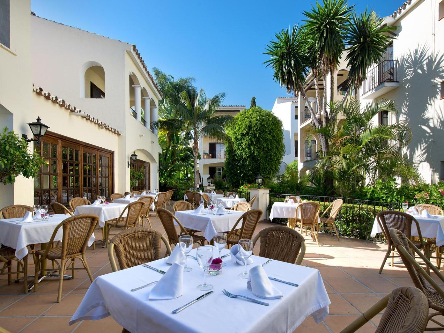 Bluebay Banus viesnīcas pagalma terase ar balti klātiem galdiņiem un tradicionālu Andalūzijas arhitektūru fonā