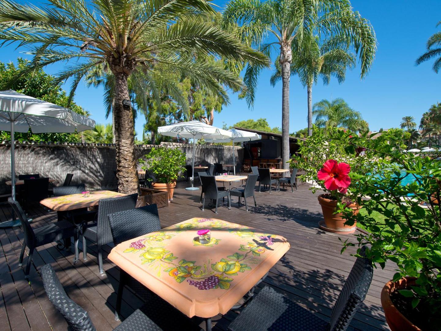 Bluebay Banus dārza terase ar dekoratīviem galdiņiem, palmām un ziedošiem augiem pie baseina zonas Marbeljā