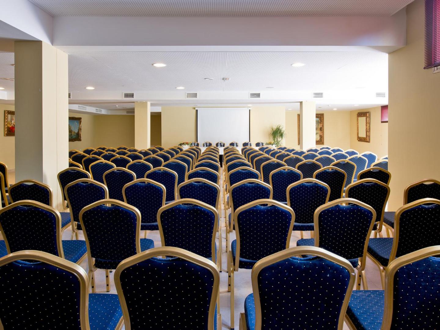 Bluebay Banus viesnīcas plašā konferenču zāle ar zilām krēsliem un prezentāciju ekrānu — piemērota vieta semināriem un pasākumiem Marbeljā.