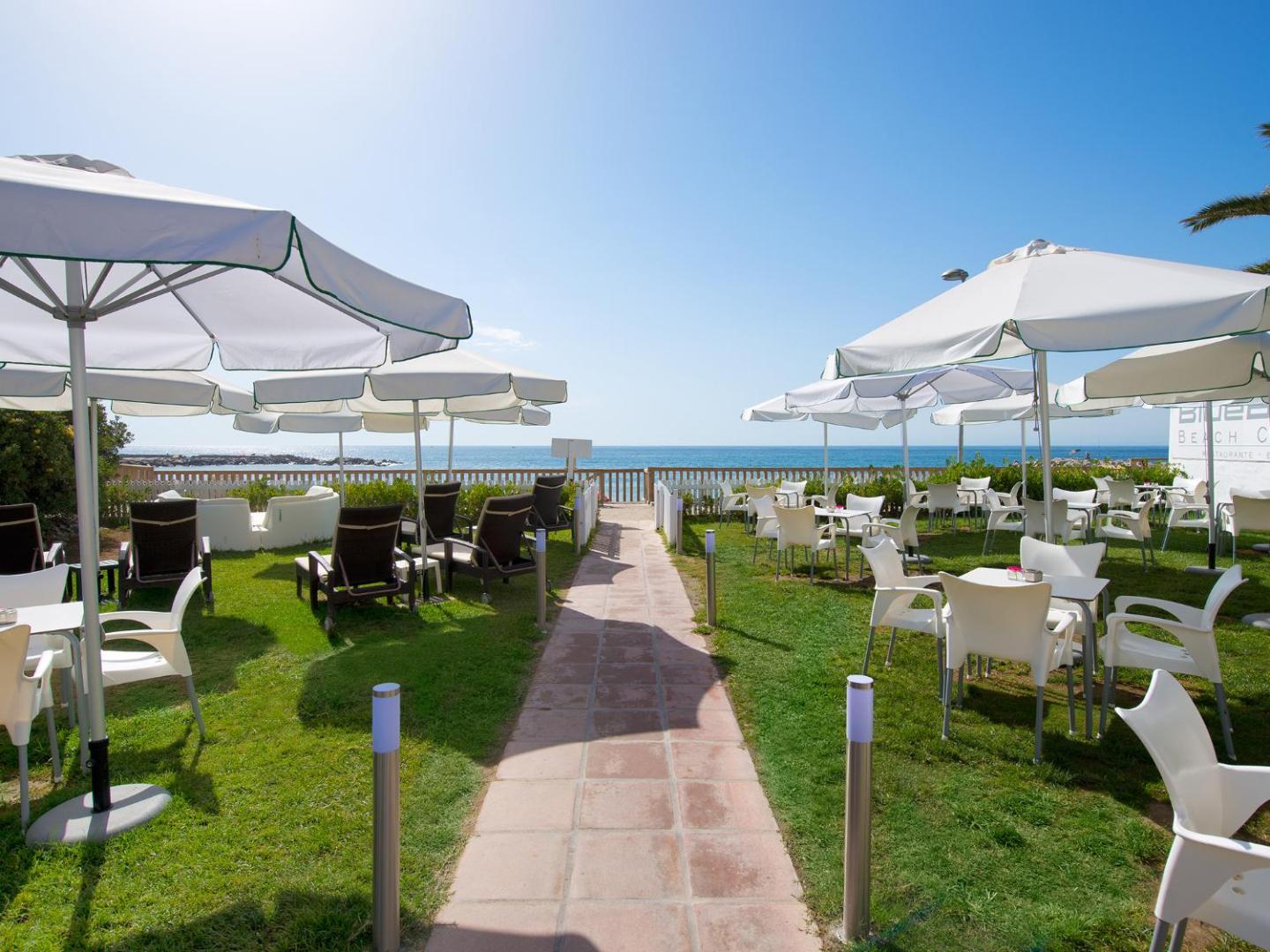 Bluebay Banus pludmales klubs ar saulessargiem, atpūtas krēsliem un skatu uz Vidusjūru Marbeljas piekrastē
