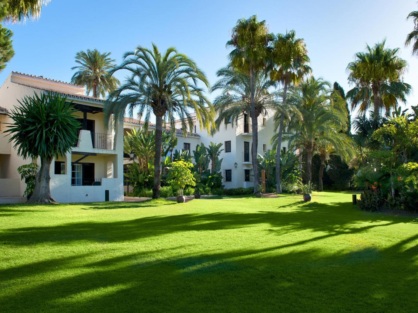 Bluebay Banus viesnīcas plašais zāliens un palmu dārzs pie baltajām numuru ēkām Marbeljas kūrortā, Spānijā