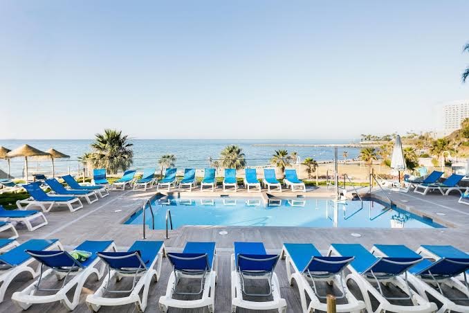Best Benalmadena āra baseins ar ziliem sauļošanās krēsliem un skatu uz jūru — plaša atpūtas zona piekrastē ar palmām.