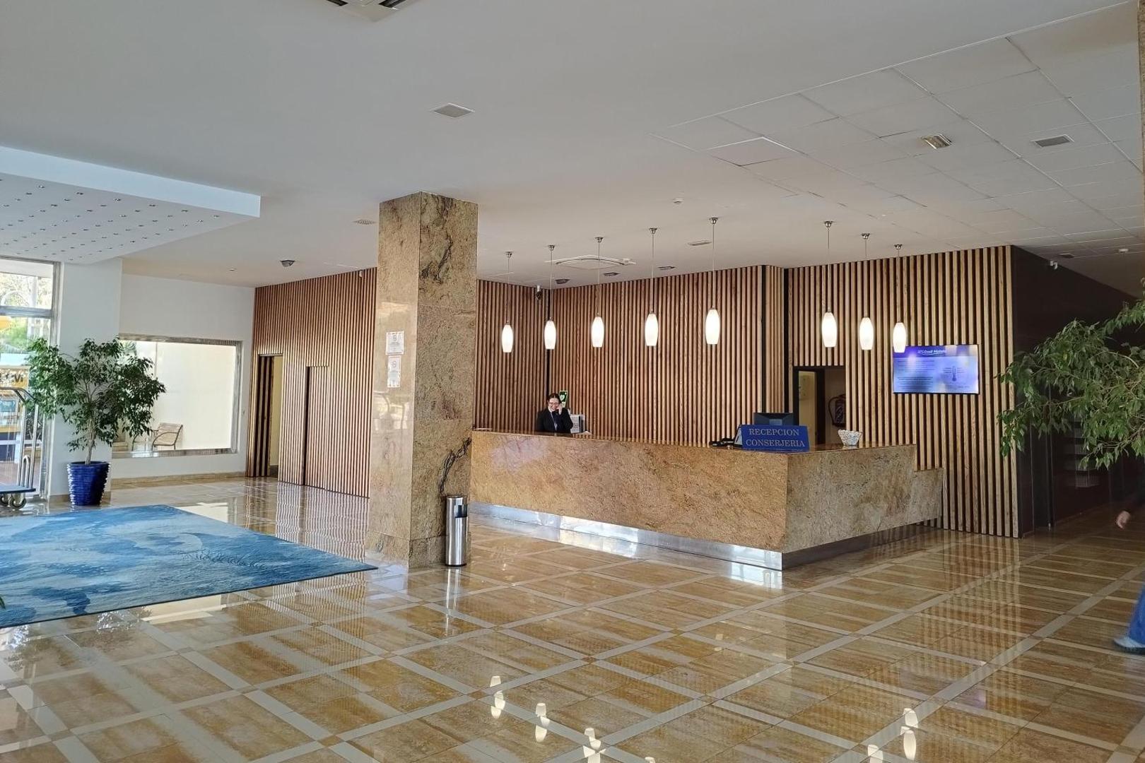Viesnīcas Best Benalmadena recepcijas zona ar marmora apdari un koka paneļu sienām — plašs vestibils ar konsjerža pakalpojumu punktu