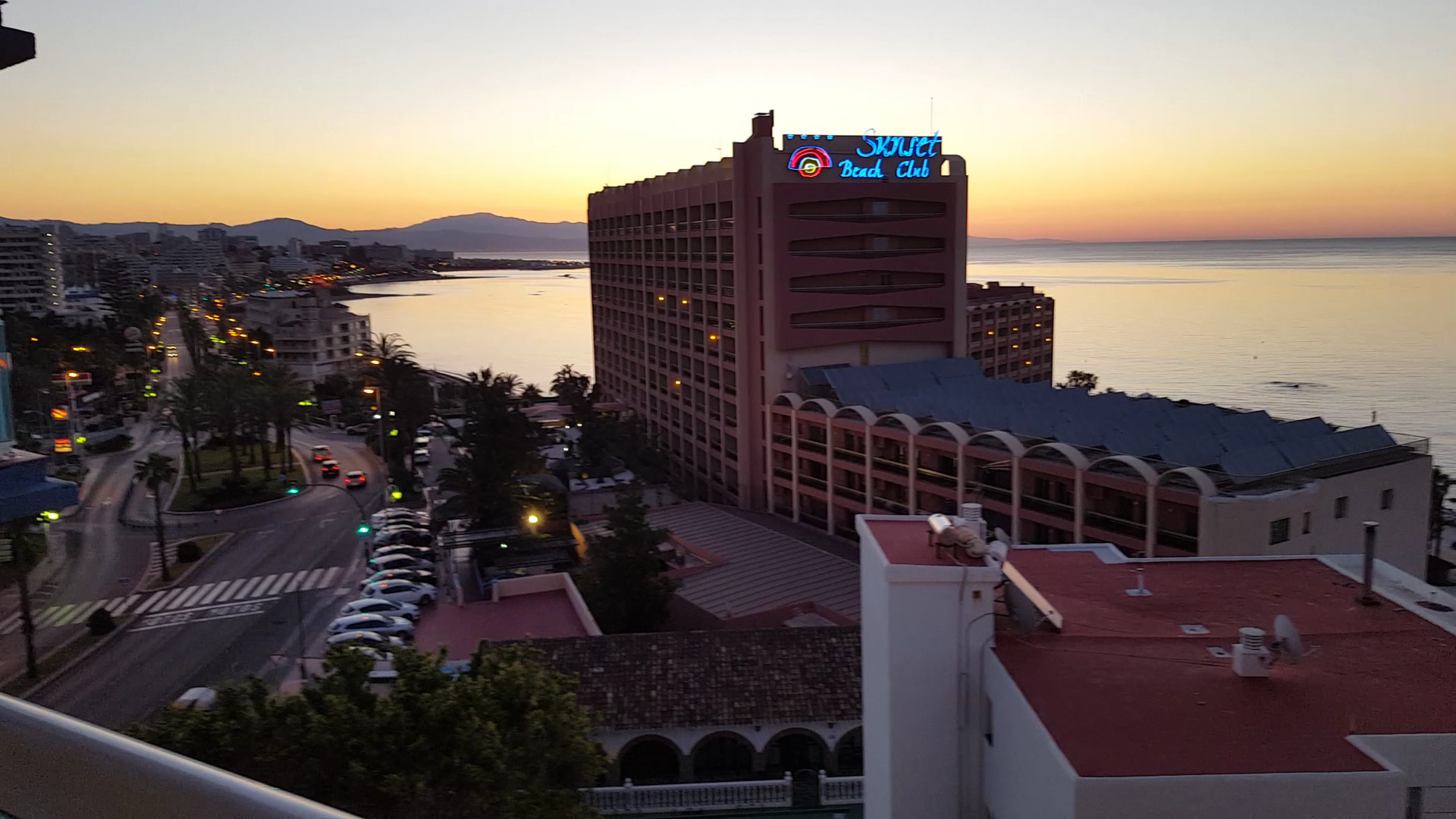 Viesnīcas Sunset Beach Club ēka saulrieta laikā Benalmadenā, skats no augšas uz pilsētas ielām un jūras līci vakarā.