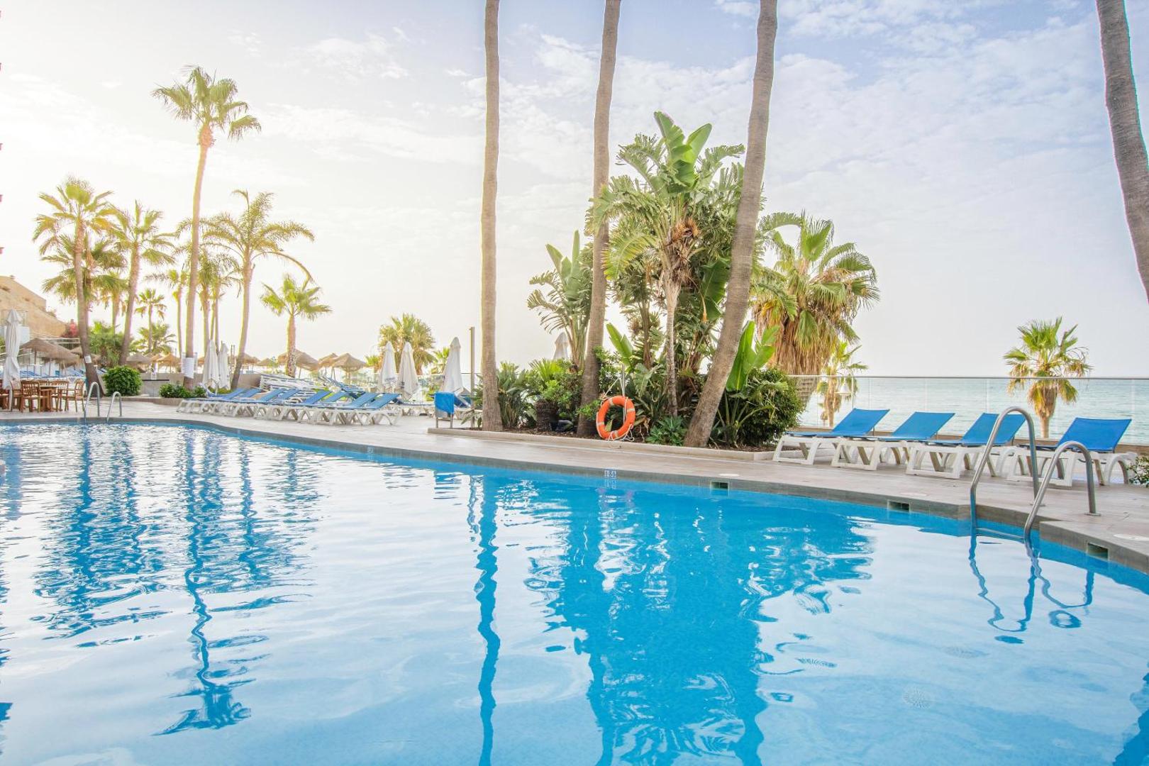 Viesnīcas Best Benalmadena baseina zona ar palmām un tropiskiem augiem — dzidrs ūdens un atpūtas krēsli saulainā pēcpusdienā.