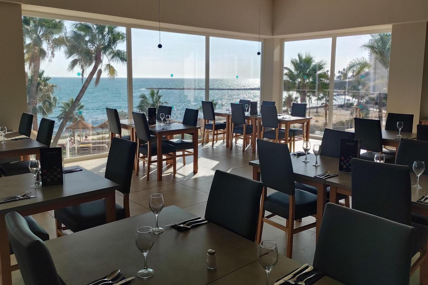 Best Benalmadena restorāna zāle ar panorāmas logiem uz Vidusjūru — galdi klāti ar vīna glāzēm un skatu uz palmām un piekrasti