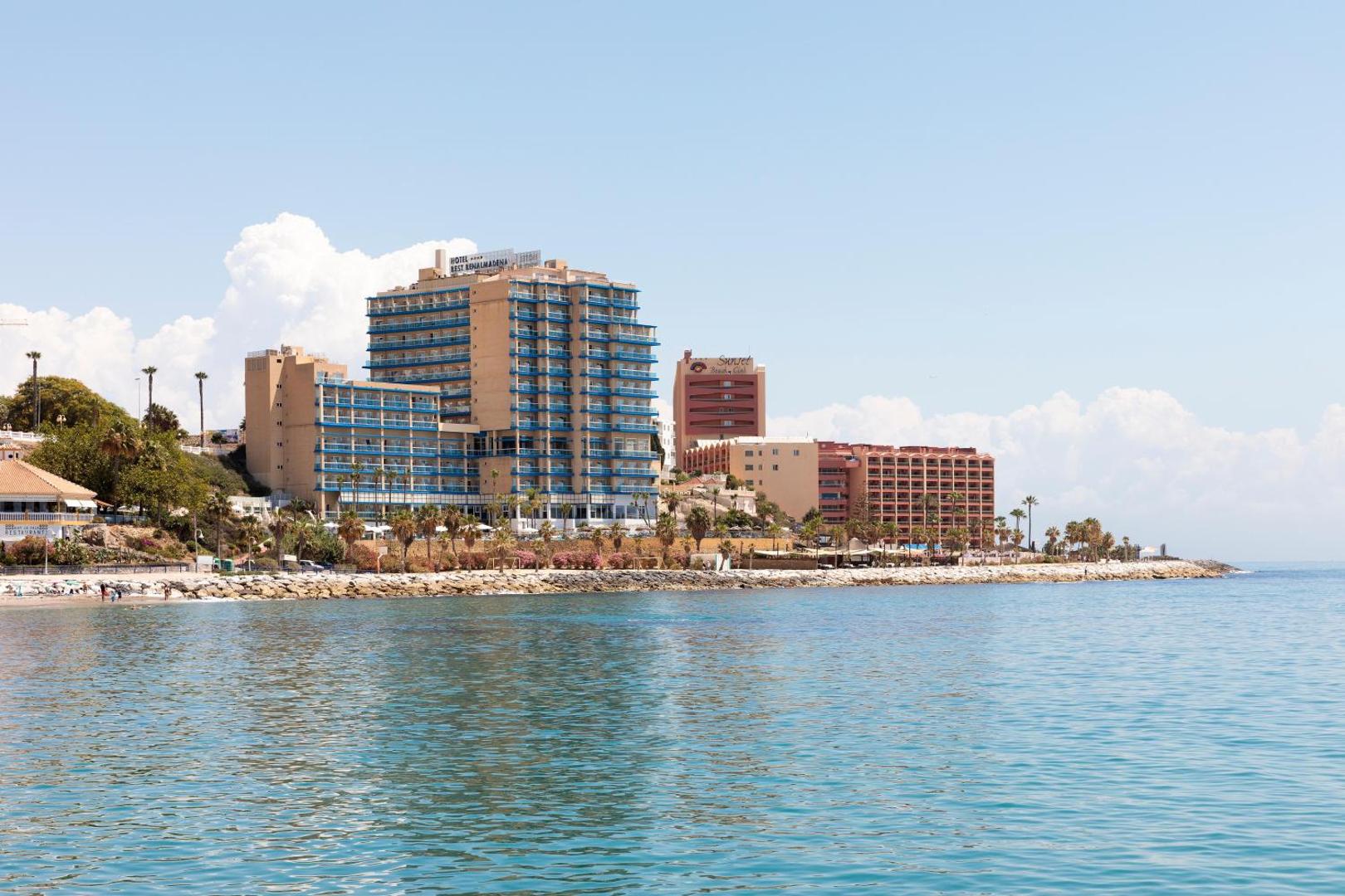 Viesnīca Best Benalmadena no jūras puses Kosta del Solā — daudzstāvu ēka pie akmeņainas piekrastes un zilā ūdens