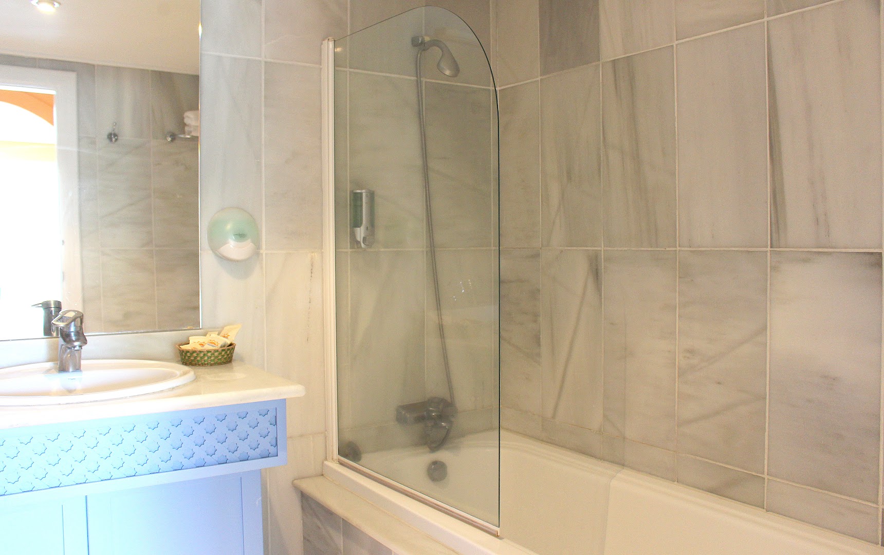 Aparthotel Monarque Sultan vannas istabas interjers ar dušas stikla sienu virs vannas un gaišām flīzēm
