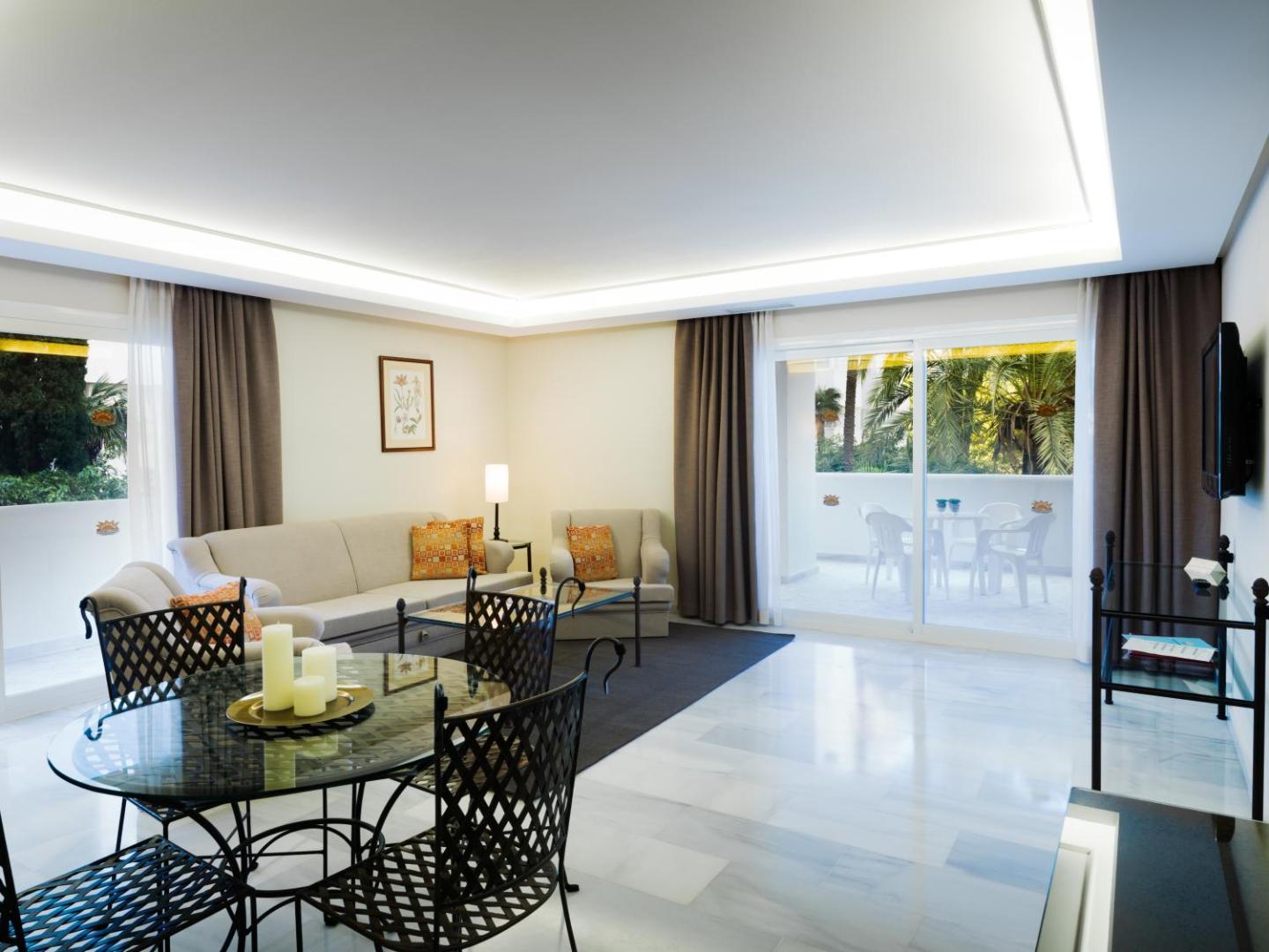Aparthotel Monarque Sultan plašs viesistabas numurs ar dīvānu, atpūtas krēsliem, ēdamgaldu un izeju uz saulainu terasi Marbeljā.