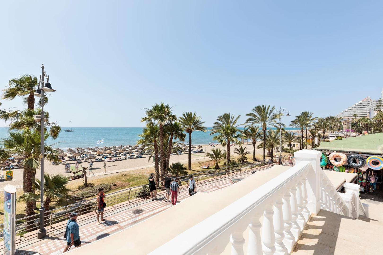 Skats no Hotel Best Triton terases uz Benalmadenas pludmali Spānijā — promenāde ar palmām, smilšu krasts un Vidusjūra saulainā dienā