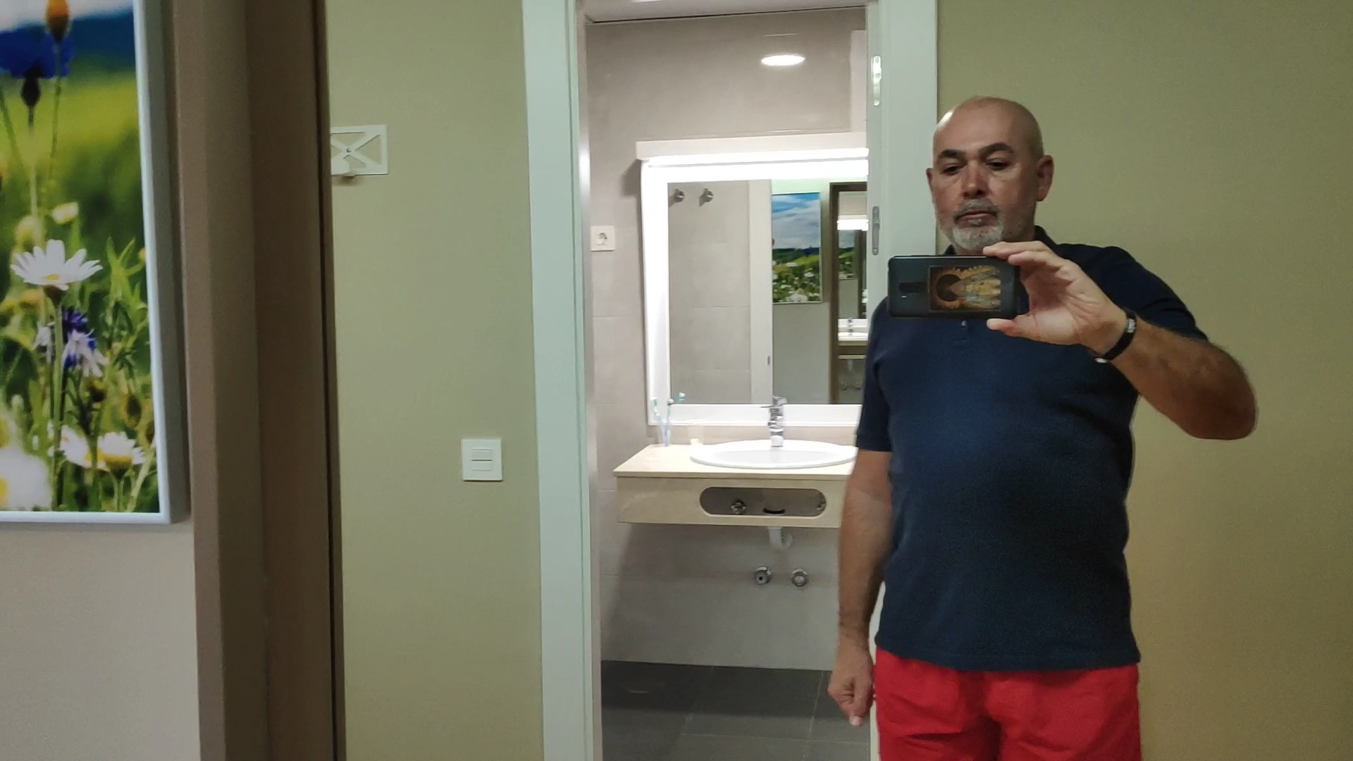 Skats uz viesnīcas Monarque Torreblanca numura vannasistabas spoguli un izlietni caur atvērtām durvīm no dzīvojamās zonas.