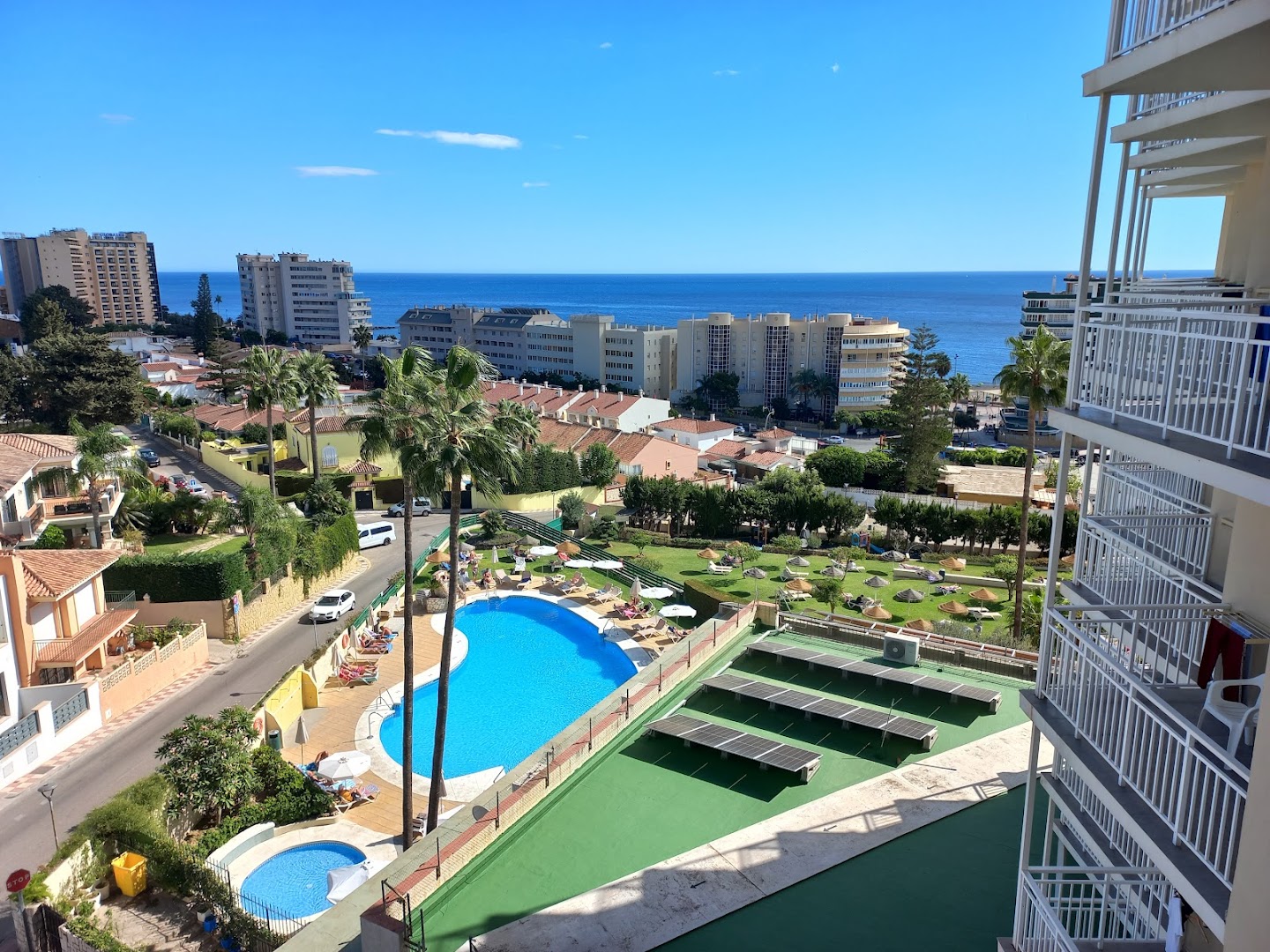 Skats no Monarque Torreblanca balkona uz āra baseinu, palmu dārzu un Vidusjūras piekrasti Fuengirolā — panorāmas skats uz pilsētu un jūru