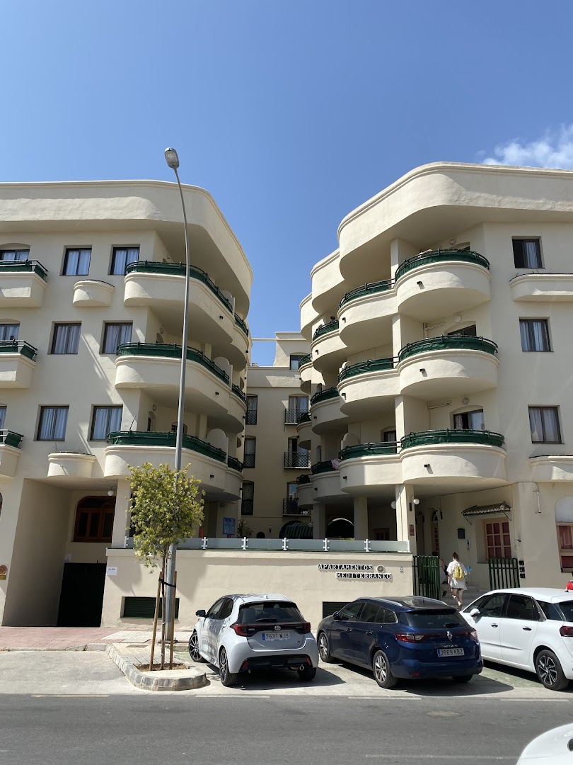 Apartamentos Mediterraneo fasādes skats ar pusapaļiem balkoniem un automašīnu stāvvietu pie ieejas saulainā dienā
