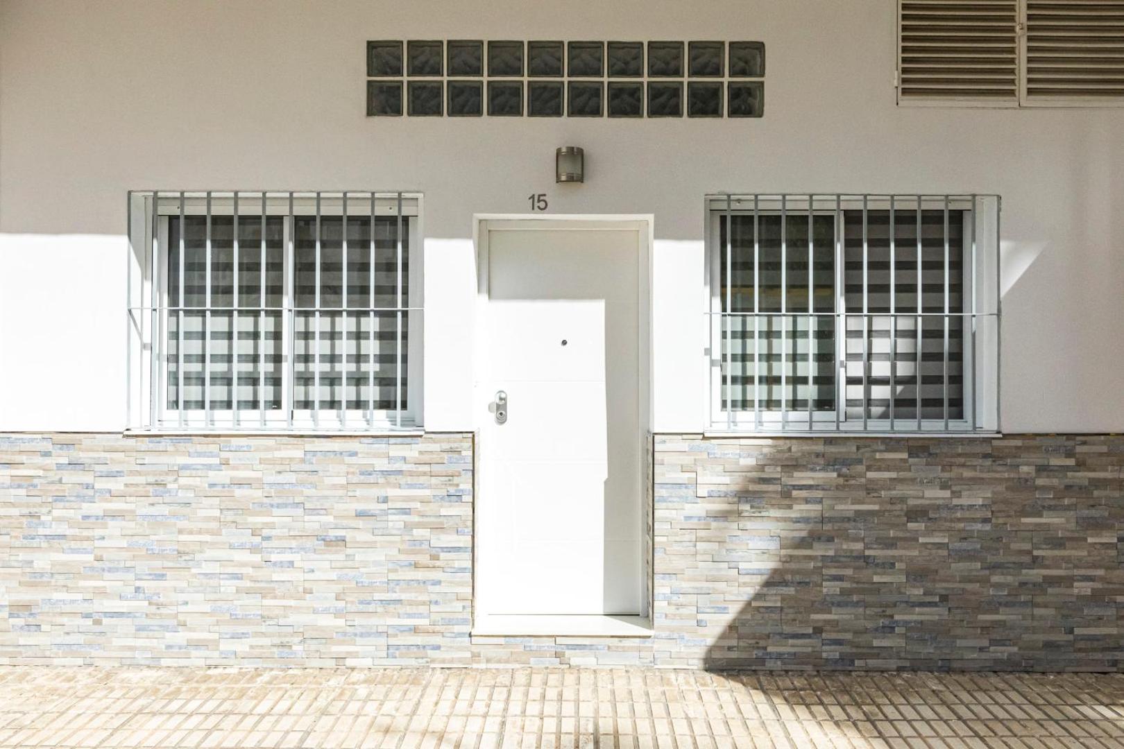 Apartamentos Mediterraneo numura ieeja ar baltām durvīm, dekoratīvu akmens apdari un aizsargrežģiem pie logiem