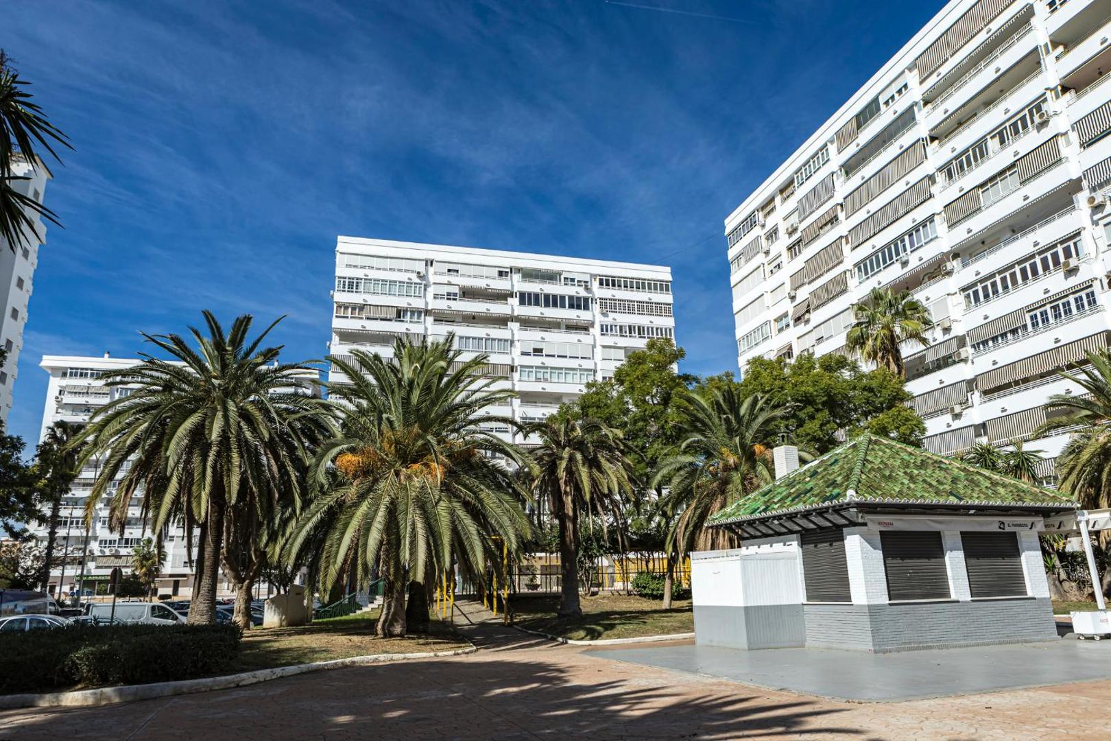 Apartamentos Mediterraneo kompleksa skats uz daudzstāvu ēkām un palmu dārzu Spānijas piekrastē saulainā dienā ar zilu debesu fonu