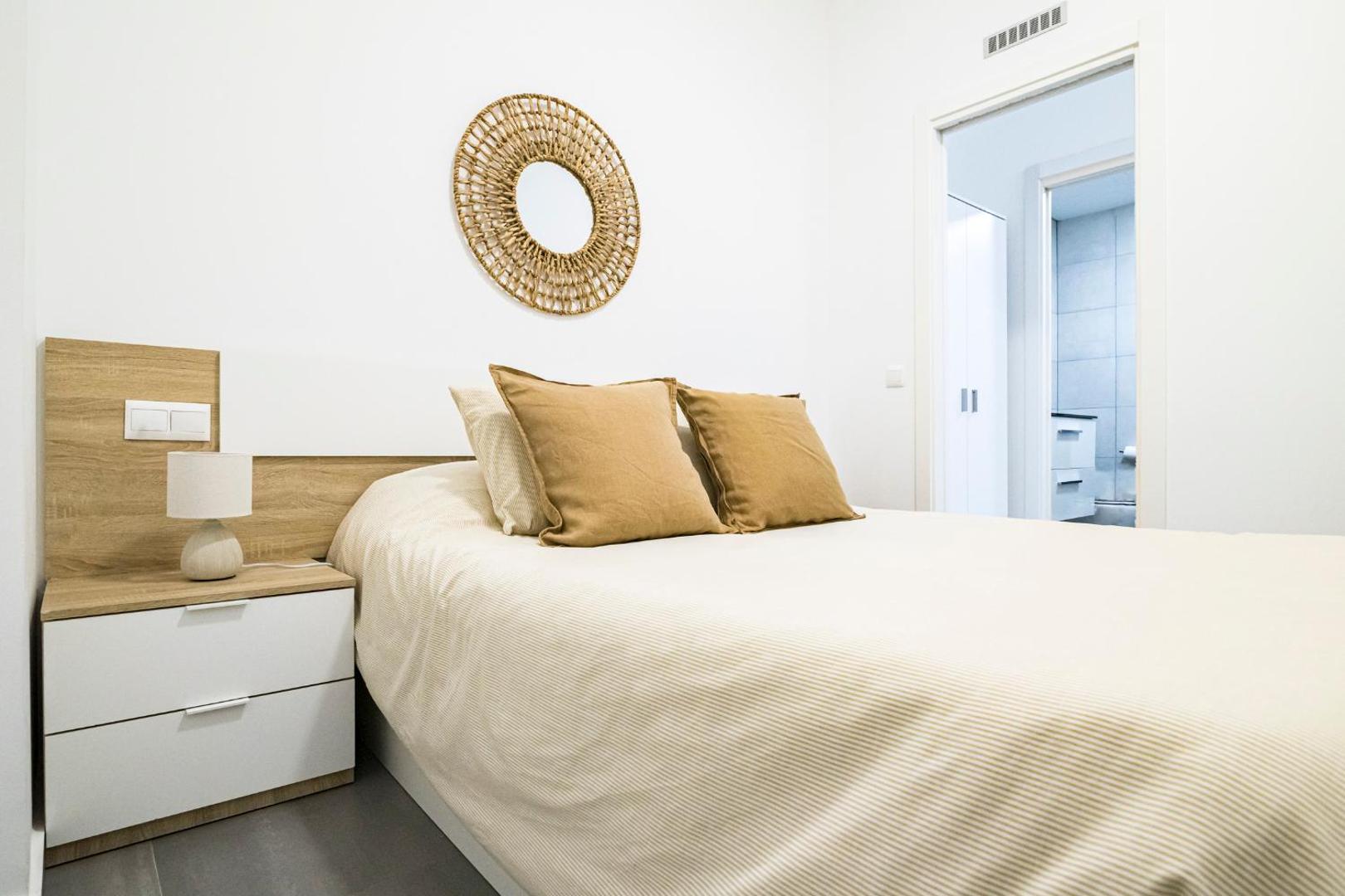 Apartamentos Mediterraneo guļamistaba ar divguļamo gultu, dekoratīvu spoguli un ieeju vannas numurā — mājīgs apgaismojums un koka detaļas