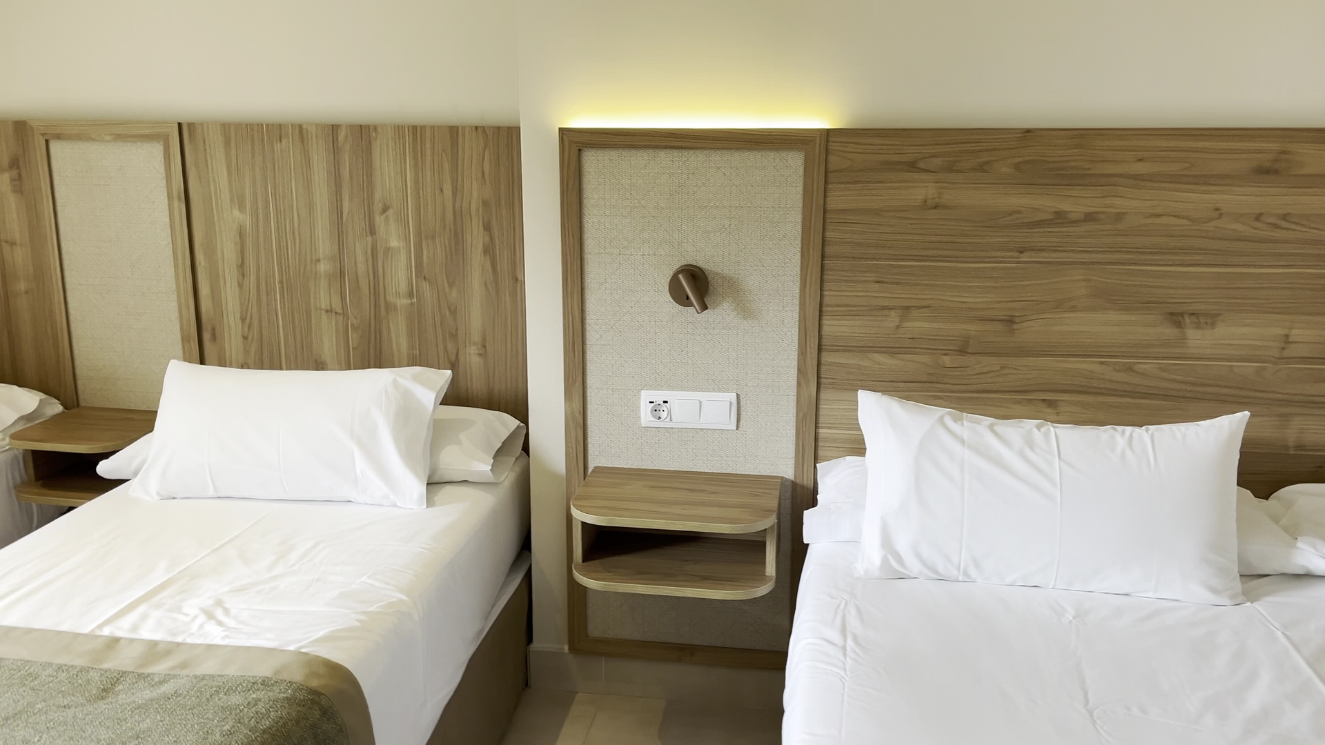 Tarik Hotel numura interjera detaļa ar divām atsevišķām gultām, koka galvgali un iebūvētu apgaismojumu pie naktsskapīša.