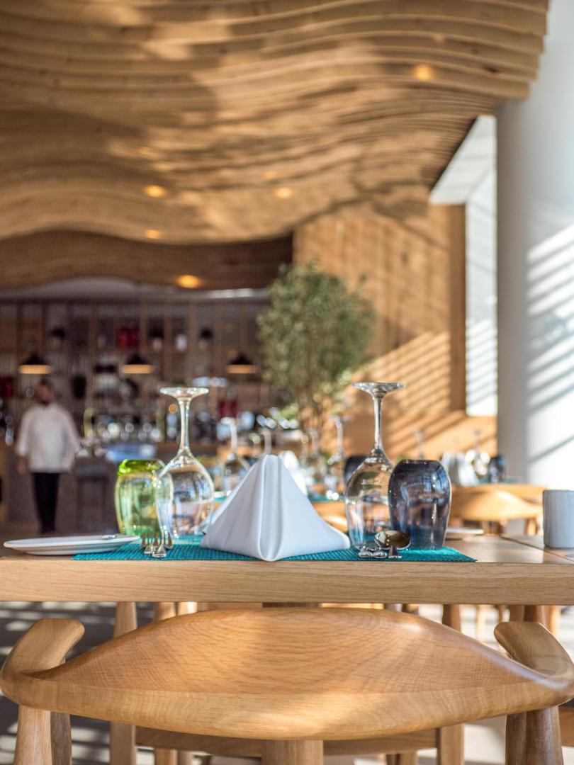 Stella Island Luxury Resort restorāna interjers ar dizaina koka griestiem un eleganti klātu galdu vakariņām Krētā