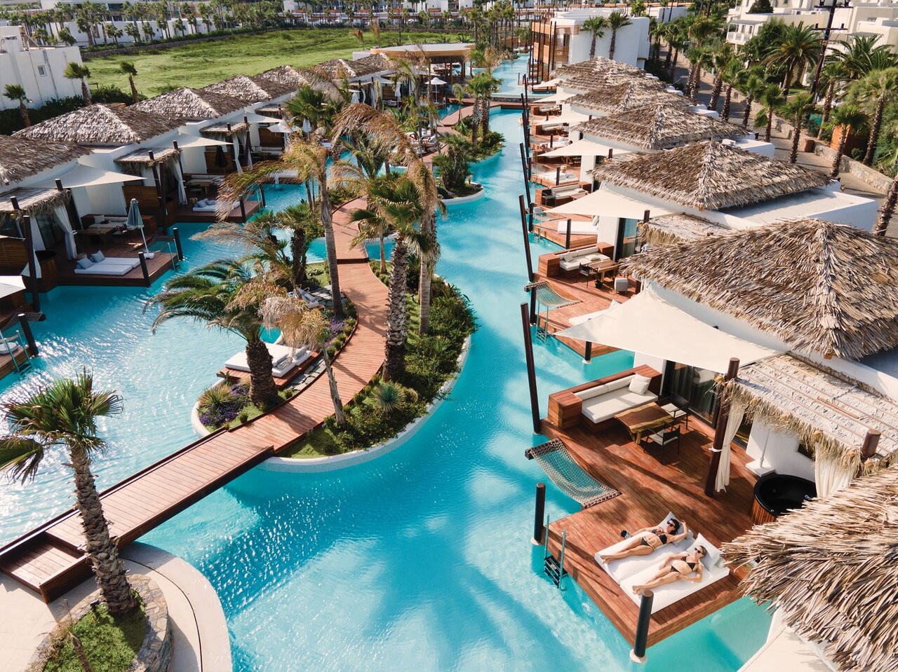 Stella Island Luxury Resort & Spa lagūnas stila baseins ar koka laipām, palmām un bungalo tipa numuriem Krētas piekrastē