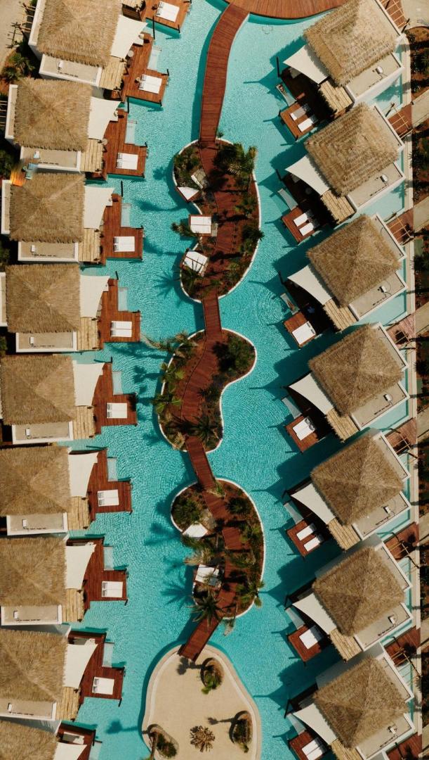 Stella Island Luxury Resort & Spa skats no augšas uz bungalo rindu pie tirkīzzila baseina ar koka terasēm un saulessargiem