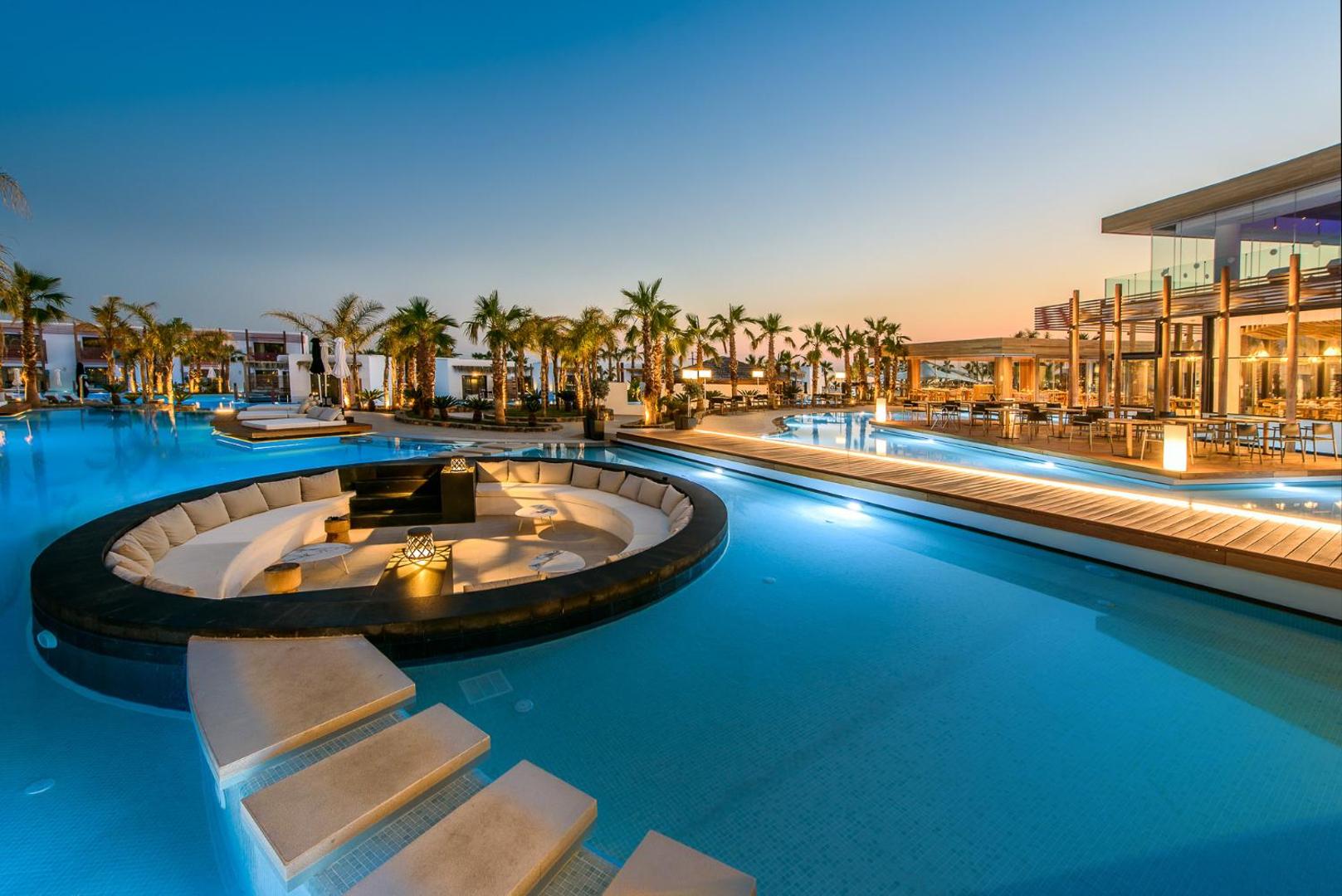 Stella Island Luxury Resort & Spa galvenais baseins saulrietā ar atpūtas zonu ūdenī un restorāna terasi Krētā