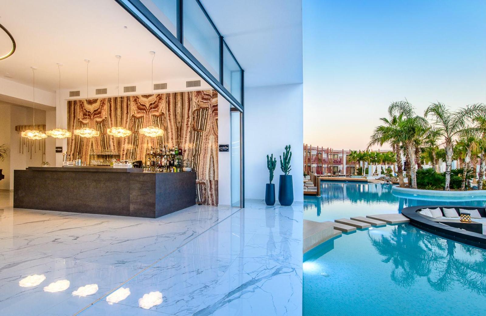 Stella Island Luxury Resort bārs pie baseina ar marmora apdari un skatu uz lagūnas tipa baseinu saulrietā