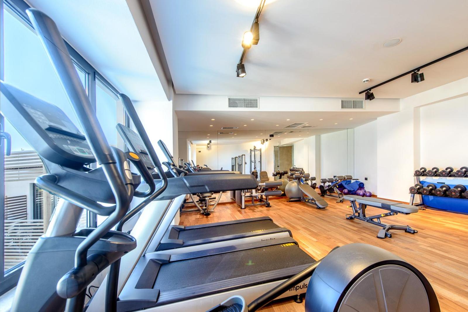 Stella Island Luxury Resort moderns fitness centrs ar skrejceliņiem un panorāmas logiem uz kūrorta teritoriju