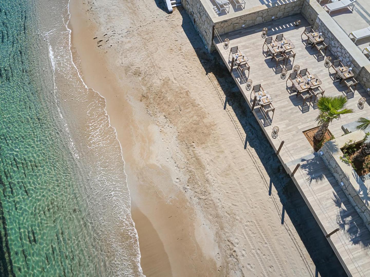 Skats no augšas uz Grecotel Lux Me White Palace āra restorāna koka terasi tieši blakus smilšu pludmalei un jūrai