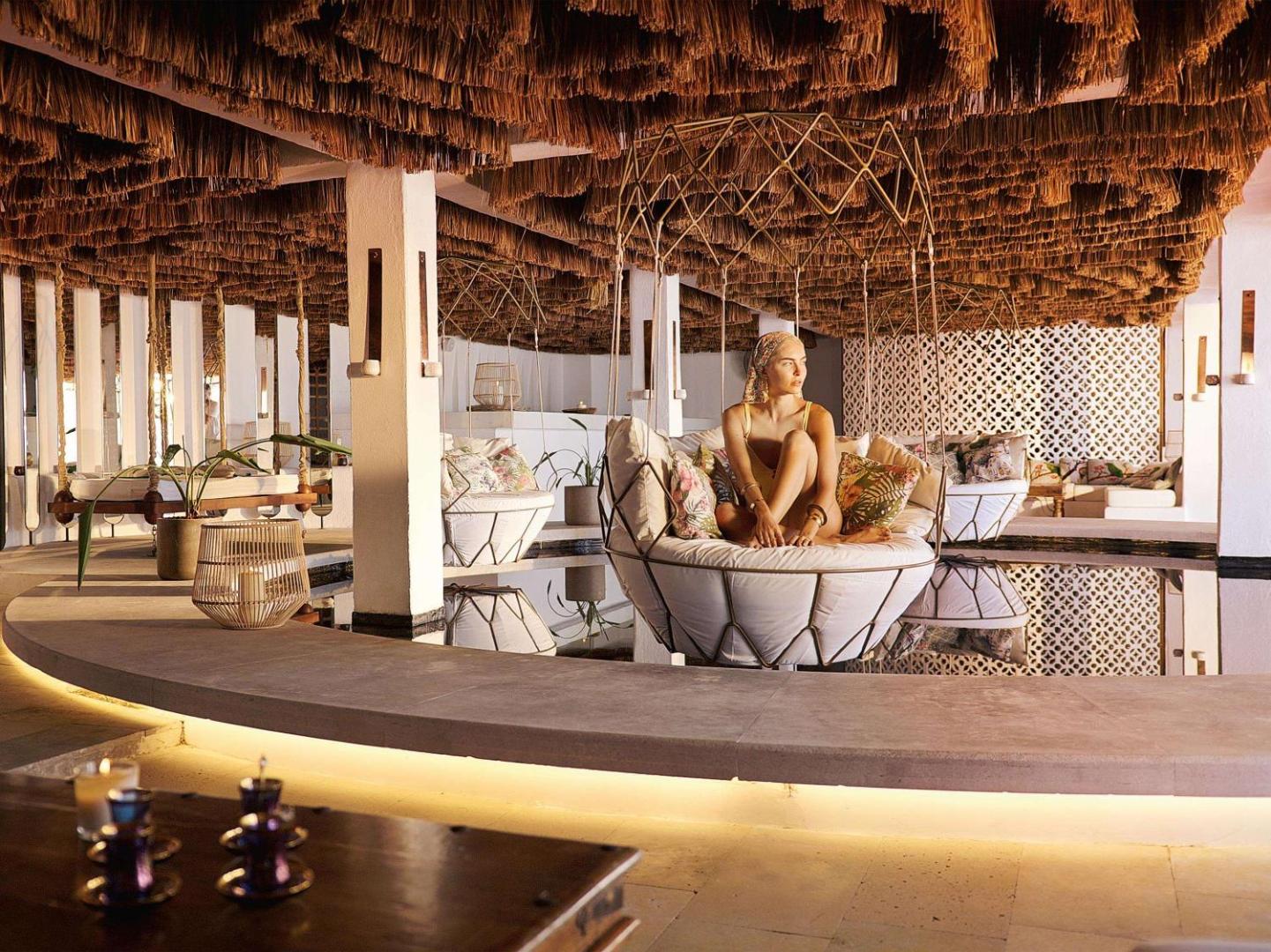 Grecotel Lux Me White Palace unikāla atpūtas zona ar iekaramiem krēsliem virs ūdens un stilīgu griestu dekoru